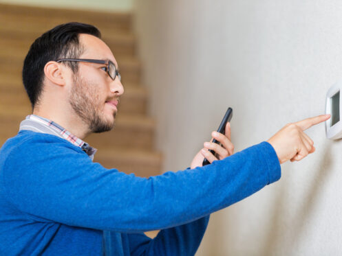 A man setting his smart thermostat with his phone